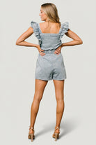 Model shot of Montgomery Denim Romper in washed blue demonstrating overall silhouette, square neckline, and short flutter sleeves for warm-weather wear.
