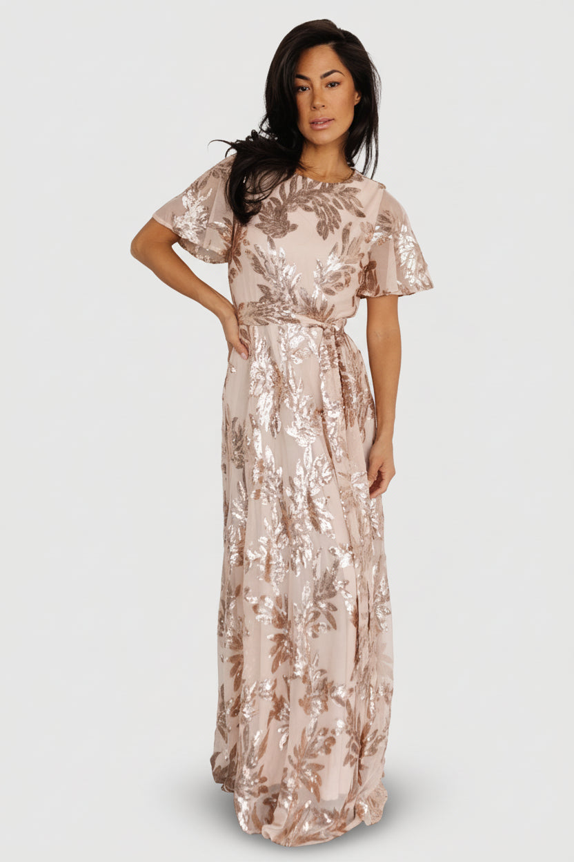 Front full-length view of a dusty pink sequin maxi dress with round neckline, waist sash, and rose-gold sequin coverage across the skirt and bodice.