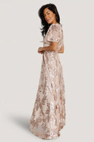 Studio image of the dress on a model highlighting the round neckline, short sheer sleeves, and the elegant silhouette created by the sash.