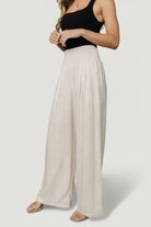 Back view of Parvati smocked waist pants in natural; high-smocked waist and flowing wide-leg hem on model.