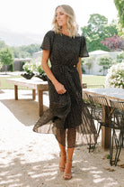 Close-up of bodice showing round neckline and button-and-keyhole back closure on the Prim Pleated Midi Dress in black floral chiffon.