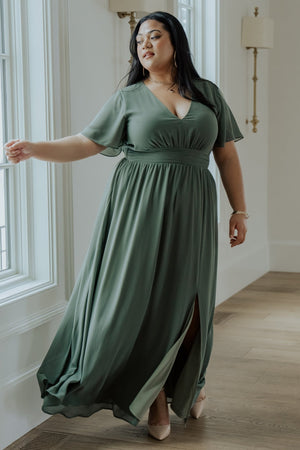 Front view of model wearing Ramona Maxi Dress in dark sage, V-neck, flutter sleeves, smocked back, left leg slit, flowing chiffon drape.