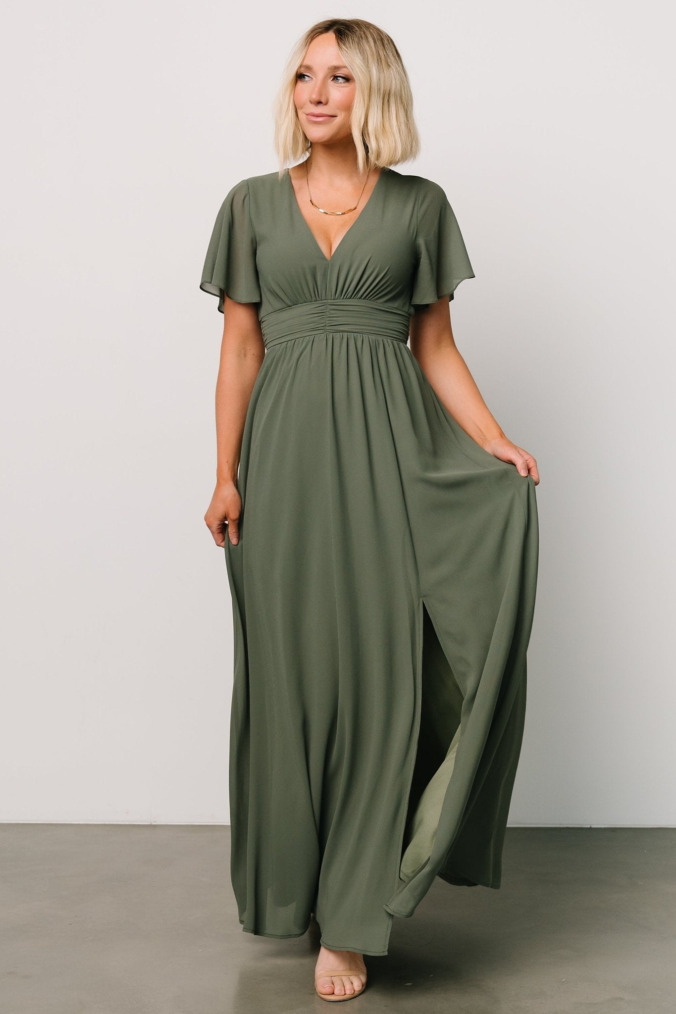Three-quarter view showing Ramona Maxi Dress in dark sage with flutter sleeves, empire ruching, and graceful chiffon movement.