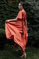 Back and side view of rust maxi dress highlighting the elasticized waistband, flowing skirt silhouette and subtle sheen of the fabric.