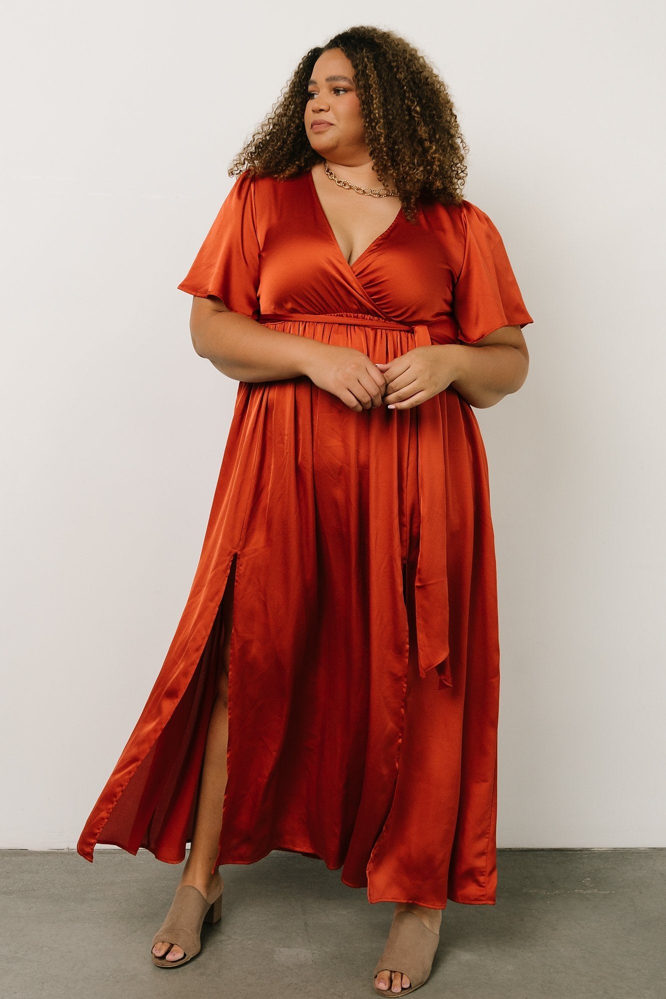 Model walking in rust satin maxi dress to show fabric drape and movement, with elastic waist and removable self-tie sash visible.