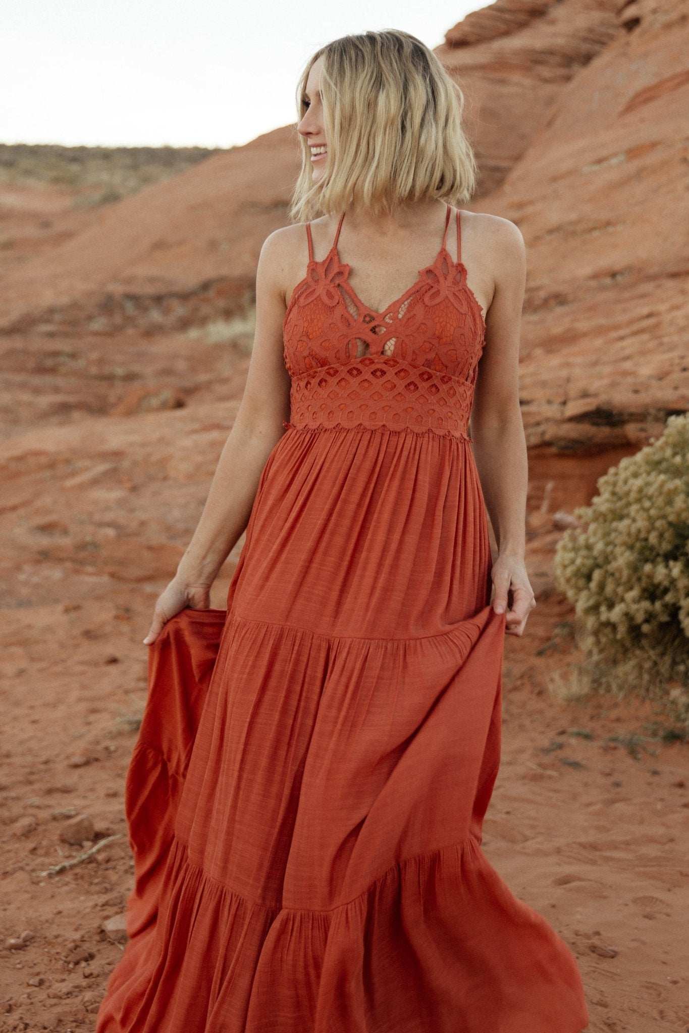Back view of rust maxi dress displaying smocked back bodice and adjustable criss-cross straps for a flexible fit.