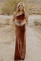Front view of bronze velvet one-shoulder maxi dress on model, fitted bodice and asymmetrical neckline, floor-length hem and subtle flare.