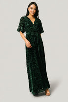 Front view of dark green Uma velvet maxi dress with burnout floral overlay, crossover surplice neckline, elastic waist, and detachable self-tie sash.